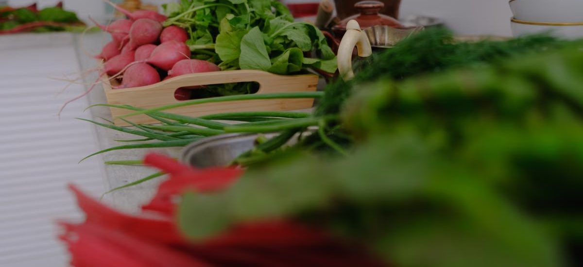 A variety of fresh vegetables including radishes and greens laid out on a kitchen countertop.